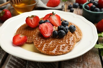 Tasty Dutch waffles (stroopwafels) with honey, strawberries and blueberries on wooden table, closeup