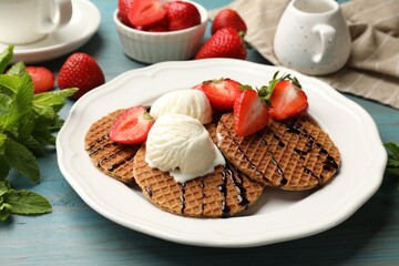 Tasty Dutch waffles (stroopwafels) with ice cream, chocolate sauce, mint and strawberries on light blue wooden table, closeup