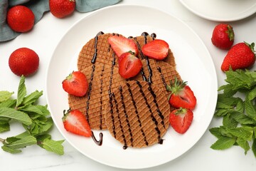 Tasty Dutch waffles (stroopwafels) with strawberries, mint and chocolate sauce on white marble table, flat lay