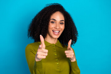 Smiling young woman pointing with both hands against blue background showcasing cheerful energy and...