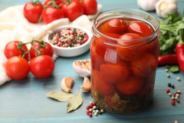 Tasty pickled tomatoes in jar and ingredients on light blue wooden table, closeup