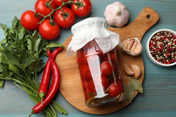 Tasty pickled tomatoes in jar and ingredients on light blue wooden table, flat lay
