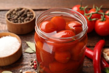 Tasty pickled tomatoes in jar and ingredients on wooden table, closeup
