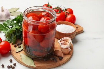 Tasty pickled tomatoes in jar and ingredients on white marble table, closeup. Space for text