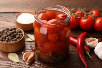 Tasty pickled tomatoes in jar and ingredients on wooden table, closeup