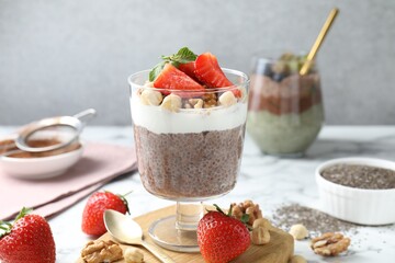 Delicious chocolate pudding with chia seeds, strawberries, yogurt and nuts in glass on white marble...