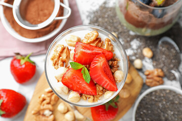 Delicious chocolate pudding with chia seeds, strawberries, yogurt and nuts in glass on white table, flat lay