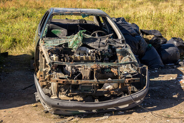 Car is in a field with a pile of trash behind it. The car is in a state of disrepair and has a...