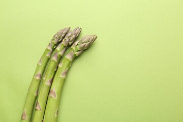 Fresh ripe raw asparagus on green background, top view. Space for text