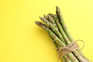 Tied raw asparagus on yellow background, top view. Space for text