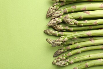 Fresh ripe raw asparagus on green background, closeup. Space for text