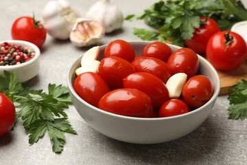 Tasty pickled tomatoes in bowl and ingredients on grey table, closeup