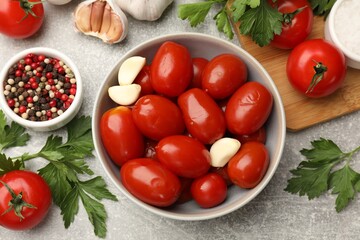 Tasty pickled tomatoes in bowl and ingredients on grey table, flat lay