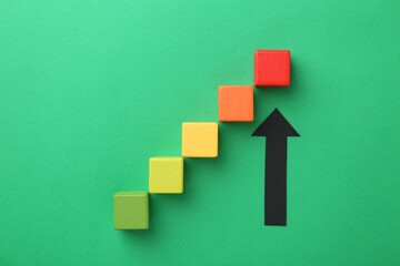 Maximum. Arrow pointing at colorful cubes on green background, flat lay