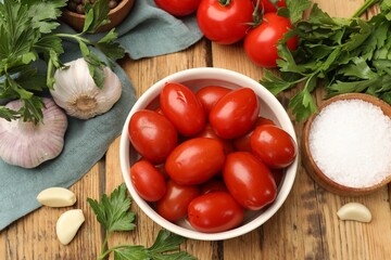 Tasty pickled tomatoes in bowl and ingredients on wooden table, flat lay