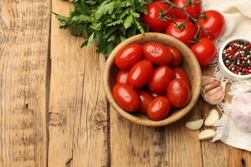 Tasty pickled tomatoes in bowl and ingredients on wooden table, flat lay. Space for text
