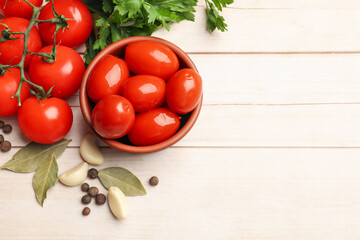 Tasty pickled tomatoes in bowl and ingredients on light wooden table, flat lay. Space for text