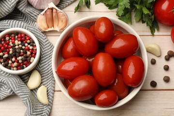 Tasty pickled tomatoes in bowl and ingredients on light wooden table, flat lay
