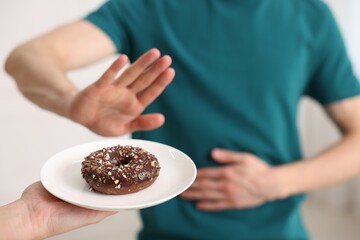 Gluten free diet. Man refusing from donut indoors, selective focus