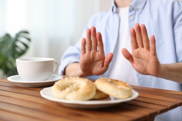 Gluten free diet. Man refusing from pastries at wooden table indoors, closeup