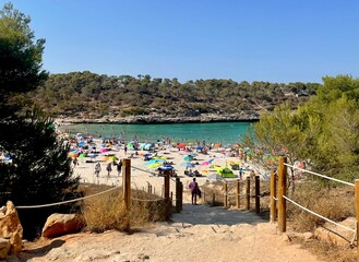 Sandy staircase leading to  white sand beach with people, colorful parasols and blue water on a...