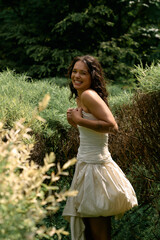 Young woman plays in a lush green garden wearing a beautiful white dress on a sunny day