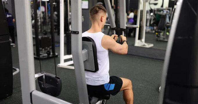 Young sportsman trains pectoral muscles on pec deck fly machine in modern gym. Focus on achieving strong physique in modern fitness center setting