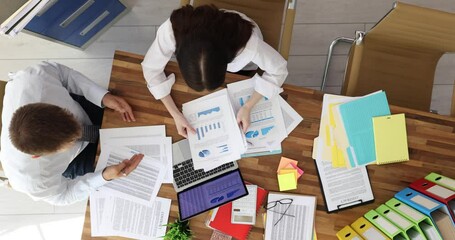 Business professionals examine financial charts and statistics at wooden desk. Collaboration on data analysis with laptop calculator and documents - Powered by Adobe