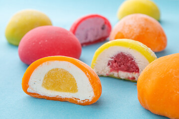 Colorful Japanese mochi desserts with various fruit and cream fillings on pastel blue background. Close-up composition ideal for food packaging, blog, menu or advertising