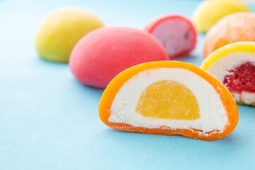 Colorful Japanese mochi desserts with various fruit and cream fillings on pastel blue background....