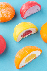 Vertical photo of colorful mochi desserts with various fruit and cream fillings on pastel blue background. Perfect for mobile content, packaging, or food design