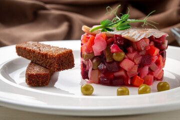 Close-up of classic Russian vinaigrette salad with diced vegetables, green peas, pickles and salted herring, served with crispy rye bread croutons. Authentic Eastern European cuisine