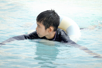 Happy Asian boy with swim ring floating on surface blue water. Relaxing kid playing with inflatable...