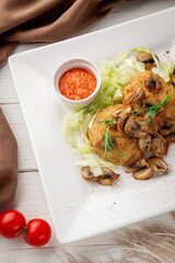 Vertical shot of golden-brown potato pancakes topped with sautéed mushrooms and onions, served with shredded lettuce and a red dipping sauce. Rustic background with cherry tomatoes