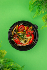 Healthy vegetable salad with cucumbers, tomatoes, bell peppers, onions and herbs in a black bowl on green background, fresh and vibrant look