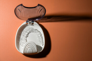 White plastic case with transparent brackets on a peach background. Invisible removable retainers...