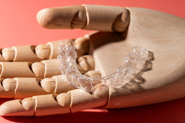 Wooden beautiful hand holds one transparent dental aligner in palms. concept of even healthy teeth