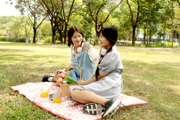 Two happy beautiful teenage girls having a picnic in park. Smiling Asian teen friends relaxing and...