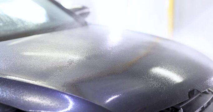 Worker applies ceramic coating evenly across surface of car hood. Experienced technician applies product with precision using sprayer. Slow motion