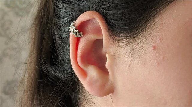 Silver cuff with precious stones in the ear of a brunette girl close-up. Earrings for pierced ears.