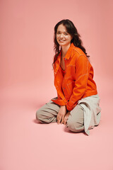Stylish young woman in vibrant orange jacket brings joy to a pastel pink setting