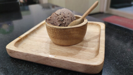 Indulgent scoop of delicious chocolate ice cream dessert in wooden bowl with spoon on tray. satisfying sweet food treat ready to eat on dark countertop