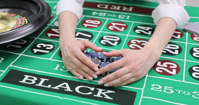 Female hands grab won chips from roulette table while choosing number field. Fingers move creating energy of gambling decision in casino slow motion