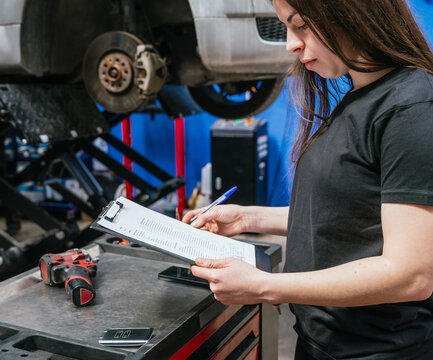 Female mechanic checking repair checklist beside lifted car in auto workshop