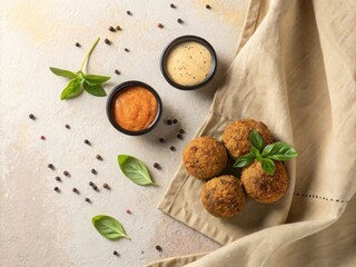 Golden brown arancini rice balls served with two dipping sauces and fresh basil leaves