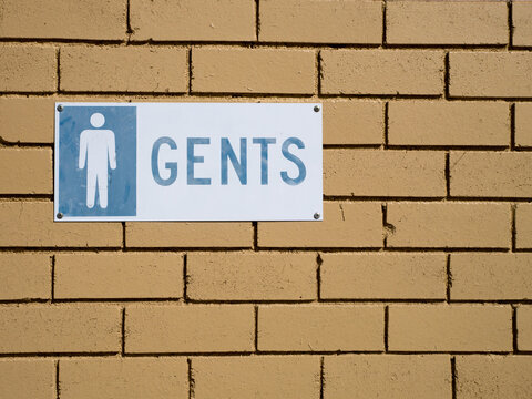 "GENTS" sign on a light coloured brick wall