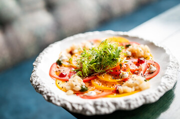 Close-up of a fresh colorful salad with tomatoes, greens, cheese, seeds, and herbs on a white plate. Healthy vegetarian dish with vibrant ingredients and gourmet presentation.