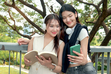 Happy two beautiful Asian women use mobile phone to take a selfie photo together outdoor in park....