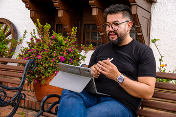 Latino man working remotely on a tablet from a colonial town in Colombia. Concepts of remote work,...