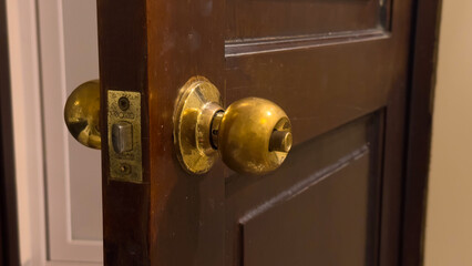 An aged brass doorknob on a dark wooden door, slightly ajar, showing wear and light reflections